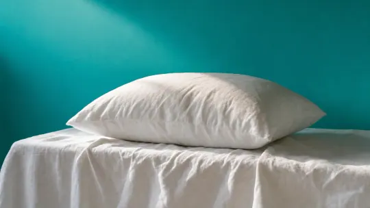 A serene bedroom shot of crisp white linens being lifted and falling gently onto a perfectly made bed in morning light